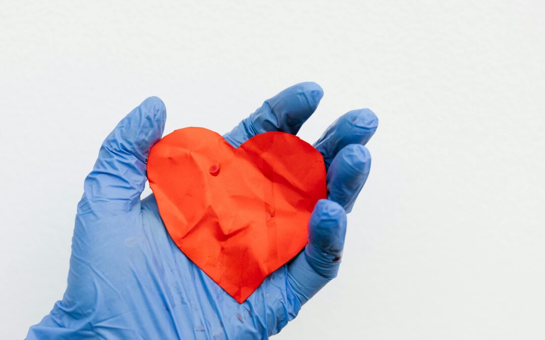 Main de chirurgien dans un gant en latex bleu portant un cœur en papier rouge illustrant un coeur qui bat vite